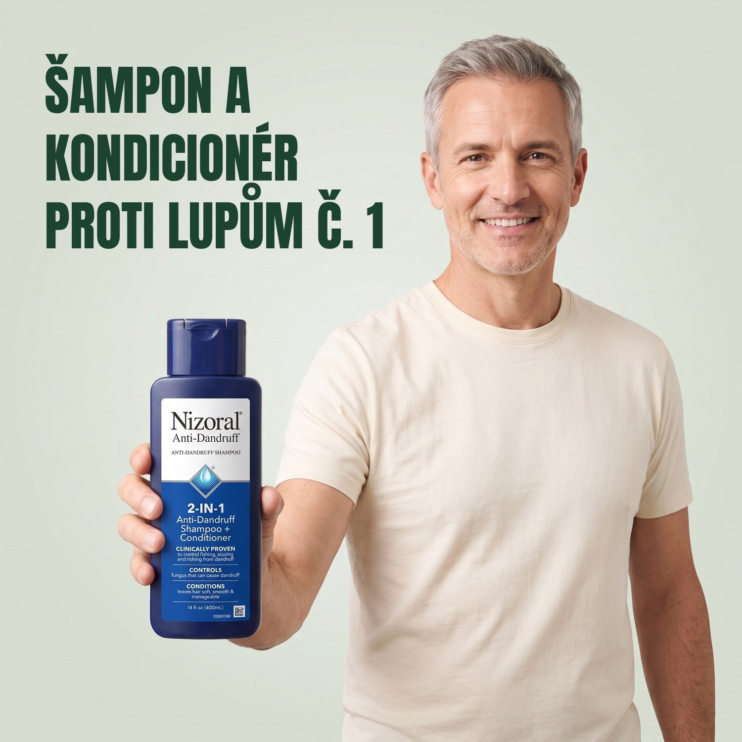 Muž drží lahvičku šamponu a kondicionéru Nizoral 2 v 1 proti lupům na zeleném pozadí