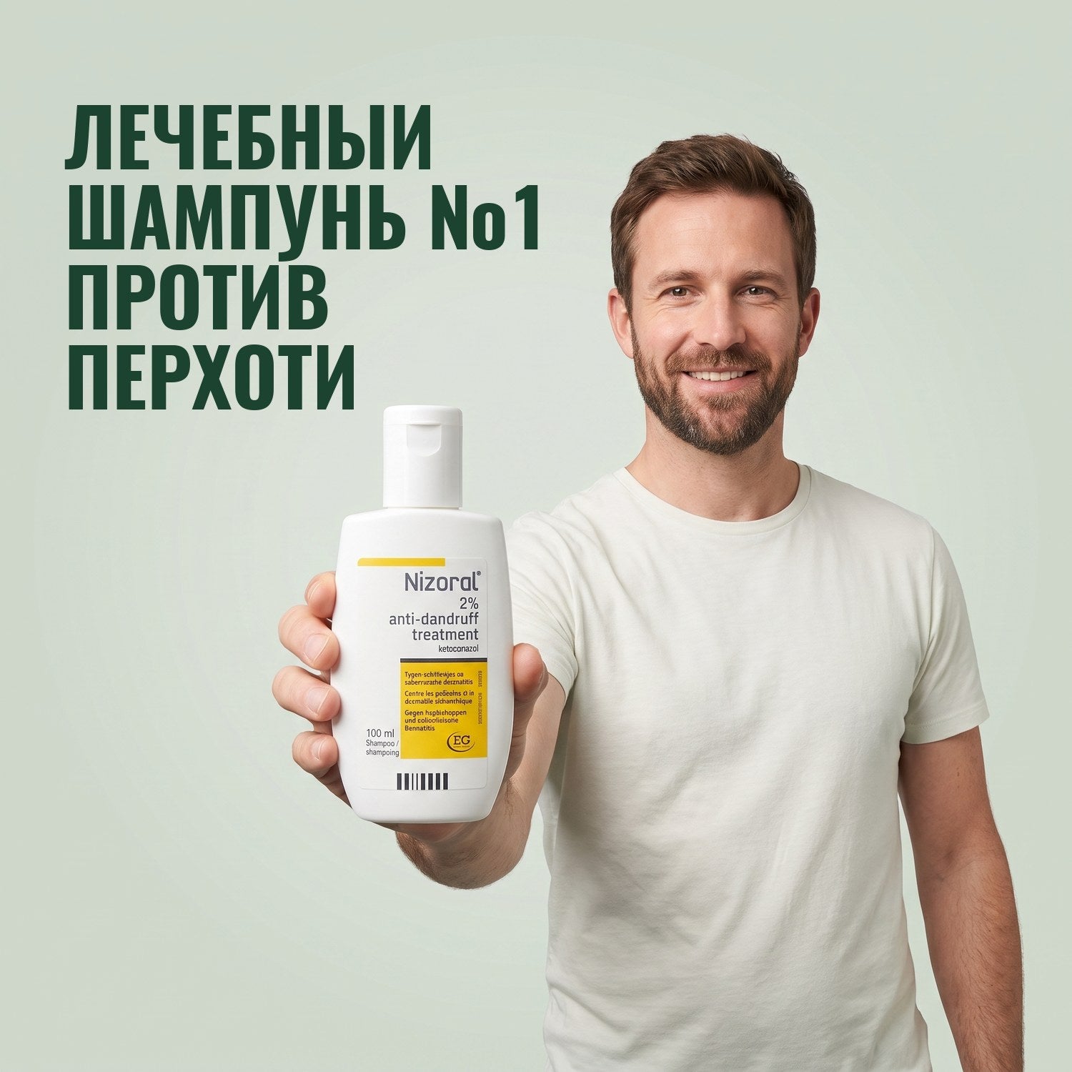 Мужчина держит флакон лечебного шампуня Nizoral против перхоти 2%, 100 мл, на зелёном фоне