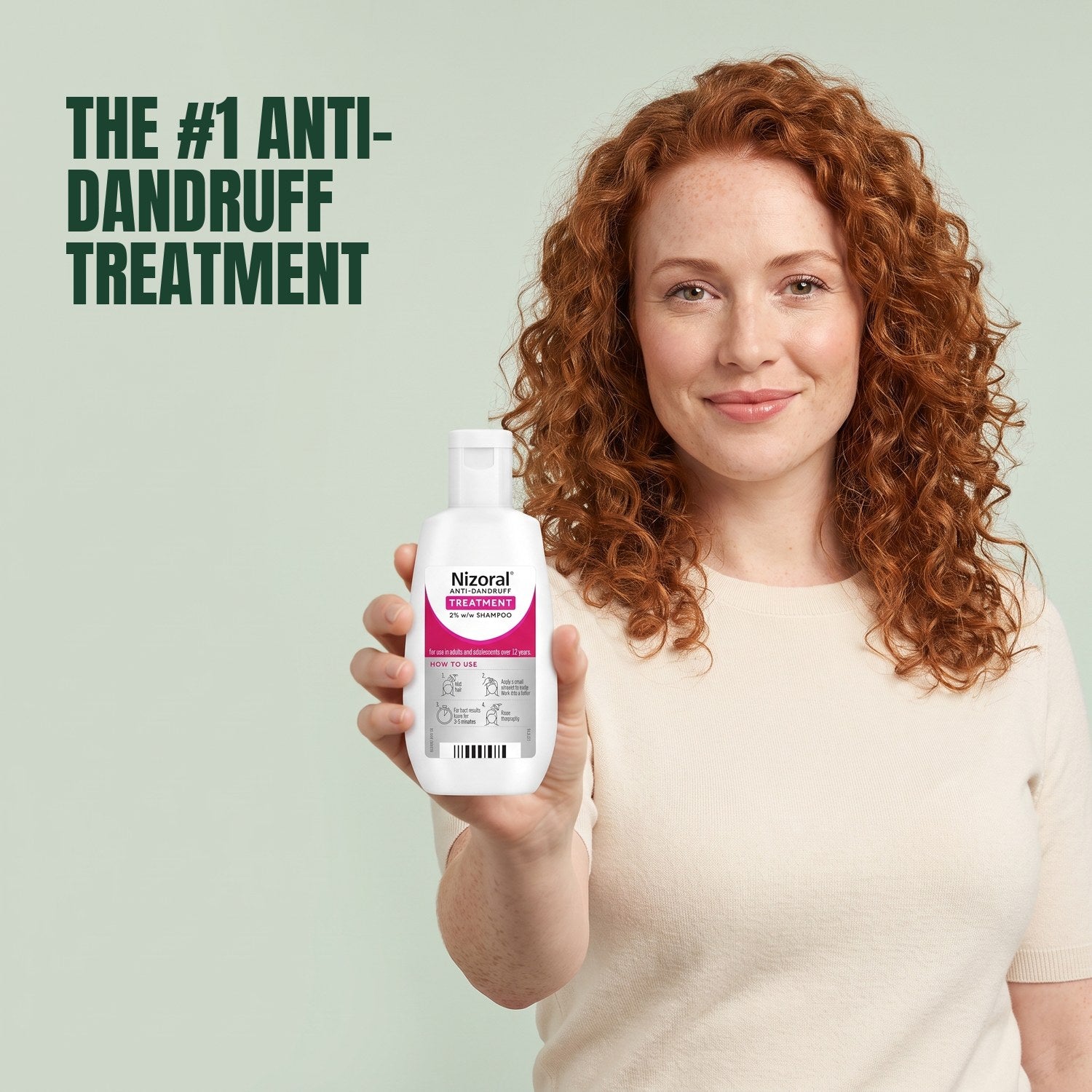 Woman holding a Nizoral anti-dandruff treatment shampoo 2% bottle against a green background