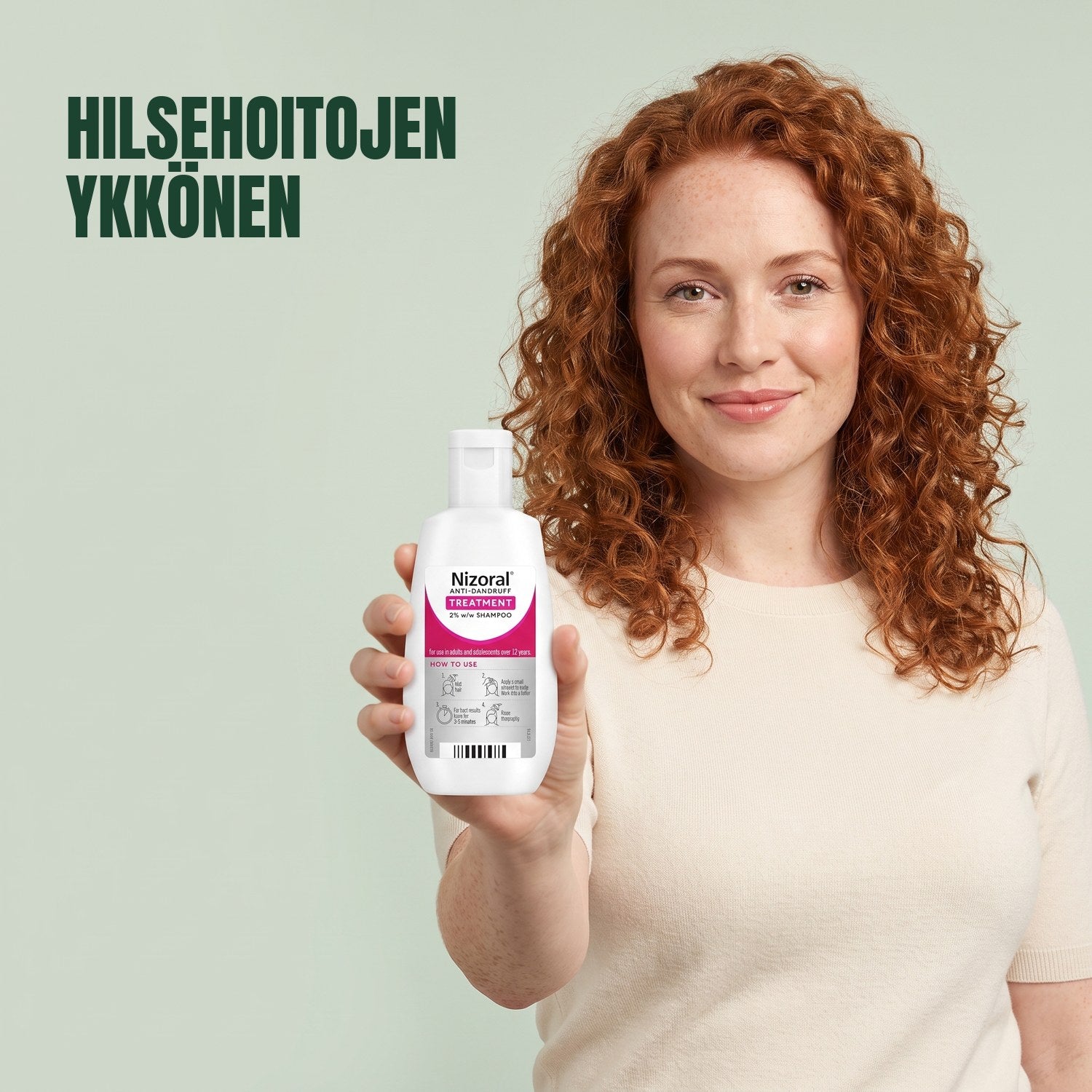 Nainen pitelee Nizoral-hilseen hoitoshampoopulloa 2% vihreää taustaa vasten
