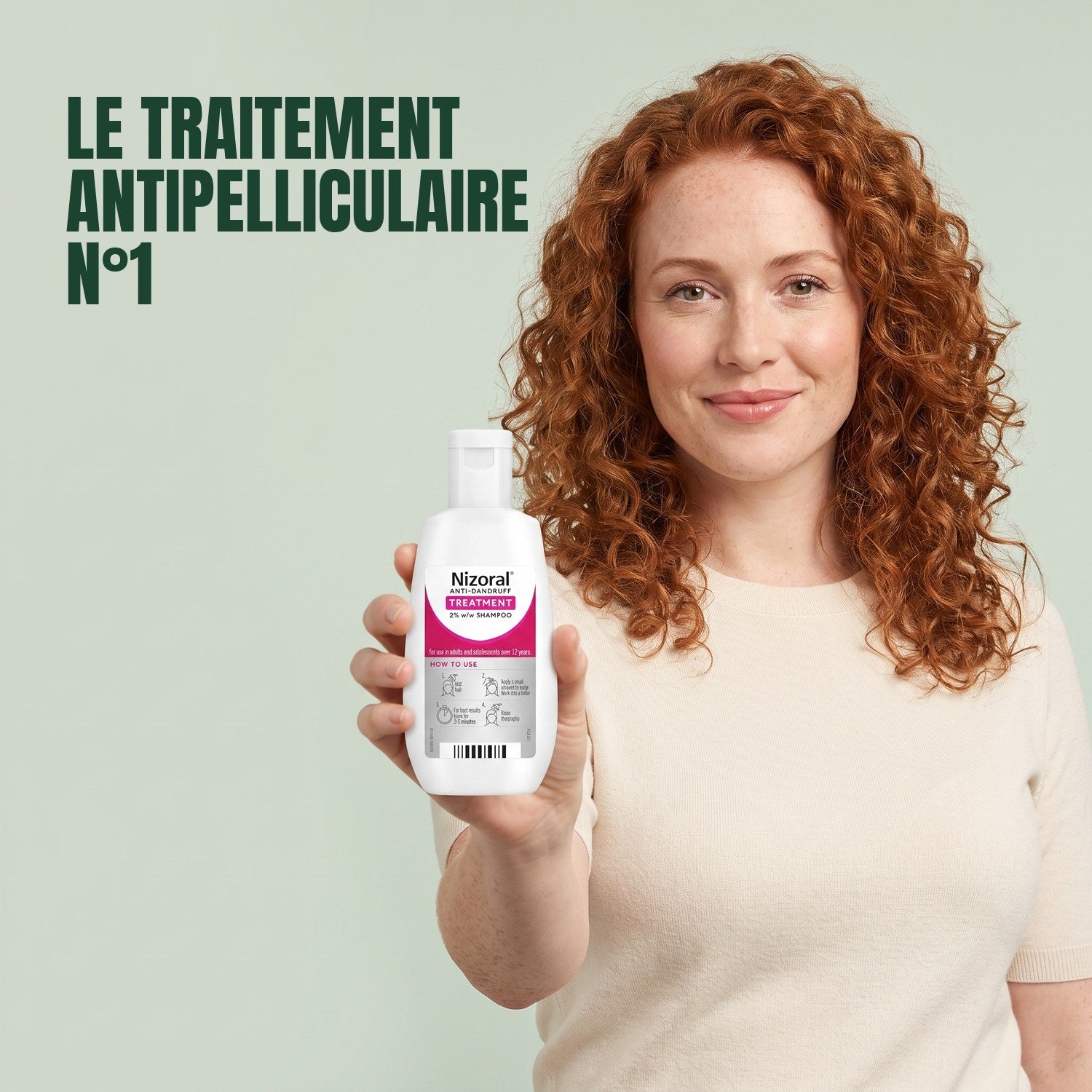 Woman holding a Nizoral anti-dandruff treatment shampoo 2% bottle against a green background