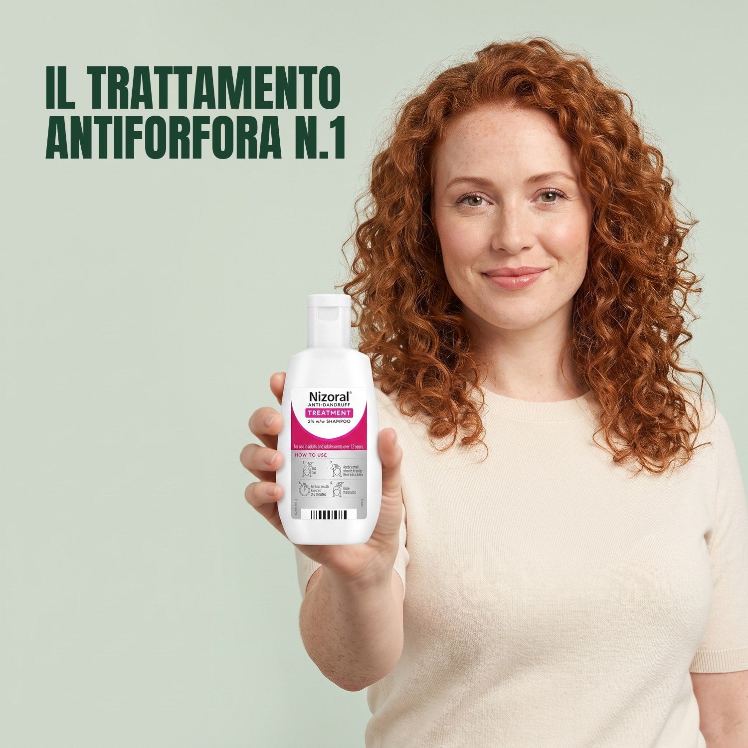 Woman holding a Nizoral anti-dandruff treatment shampoo 2% bottle against a green background