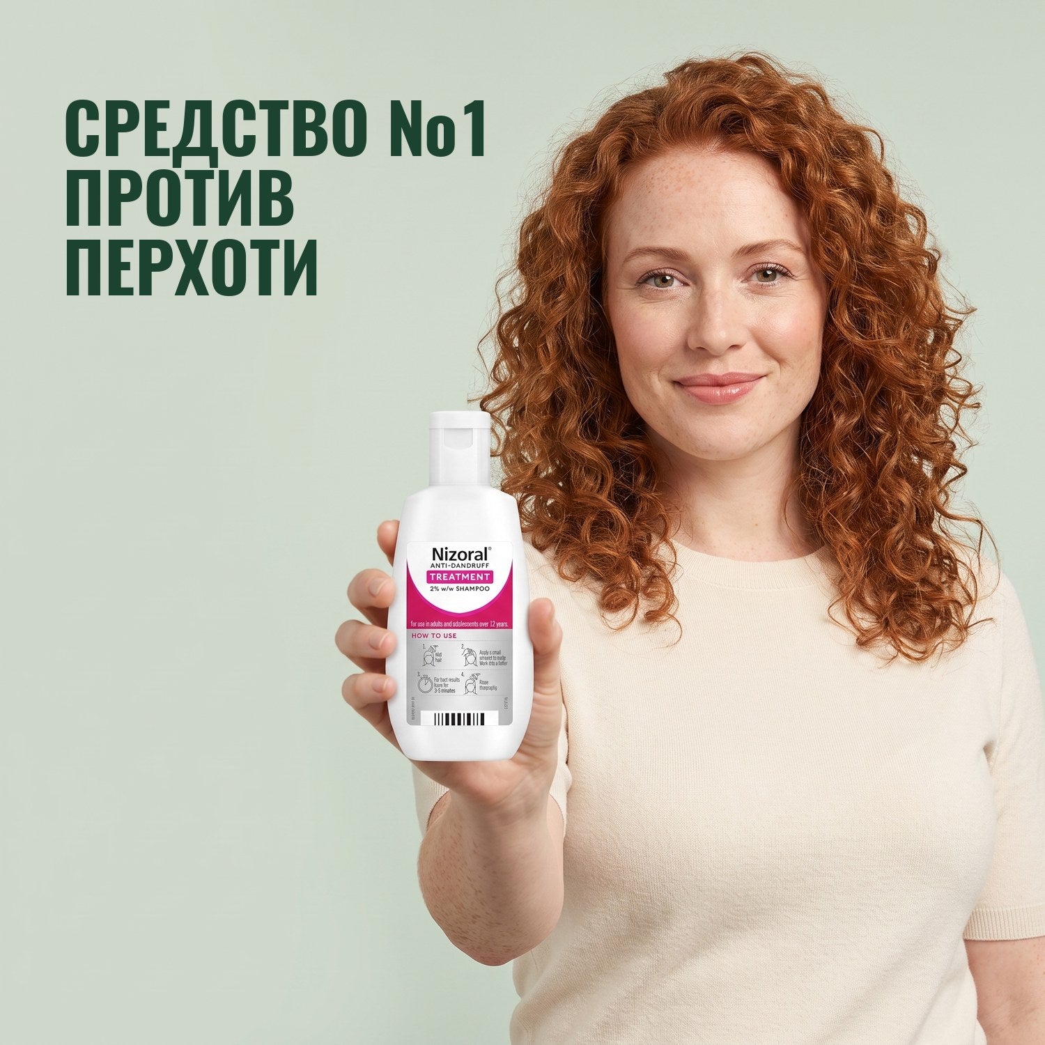 Женщина держит флакон лечебного шампуня Nizoral против перхоти 2% на зелёном фоне
