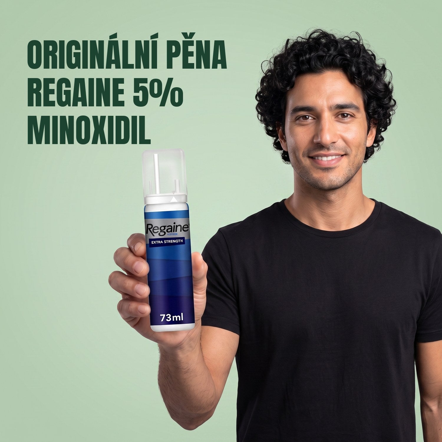 Muž drží balení pěny Regaine for Men Minoxidil 5% na zeleném pozadí