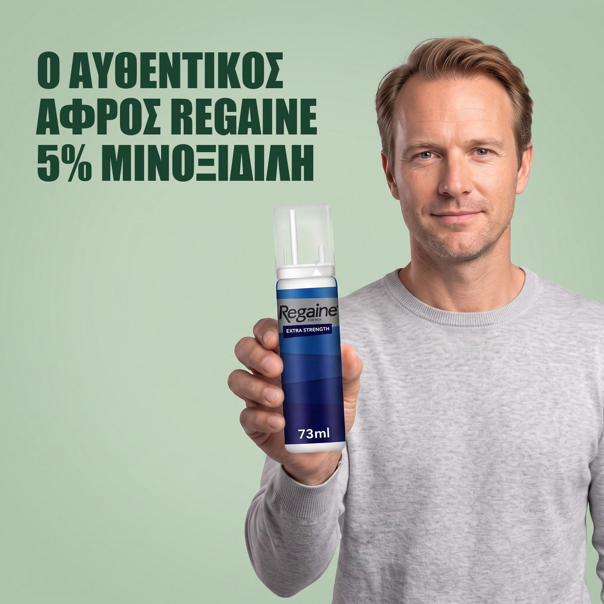 Άντρας κρατά τη συσκευασία Regaine for Men Minoxidil 5% αφρός σε πράσινο φόντο