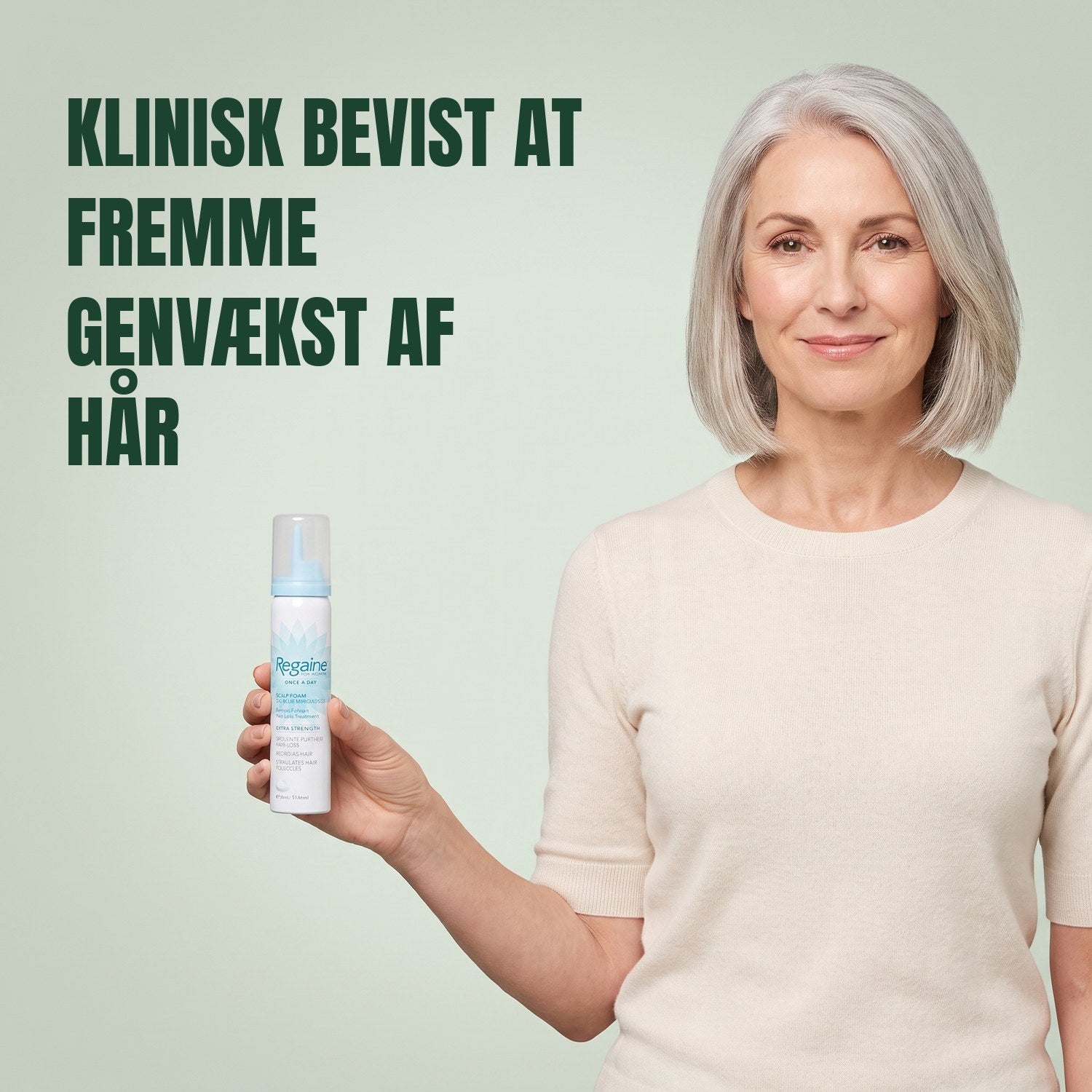 Kvinde holder en Regaine for Women Minoxidil 5% skumdåse mod en grøn baggrund