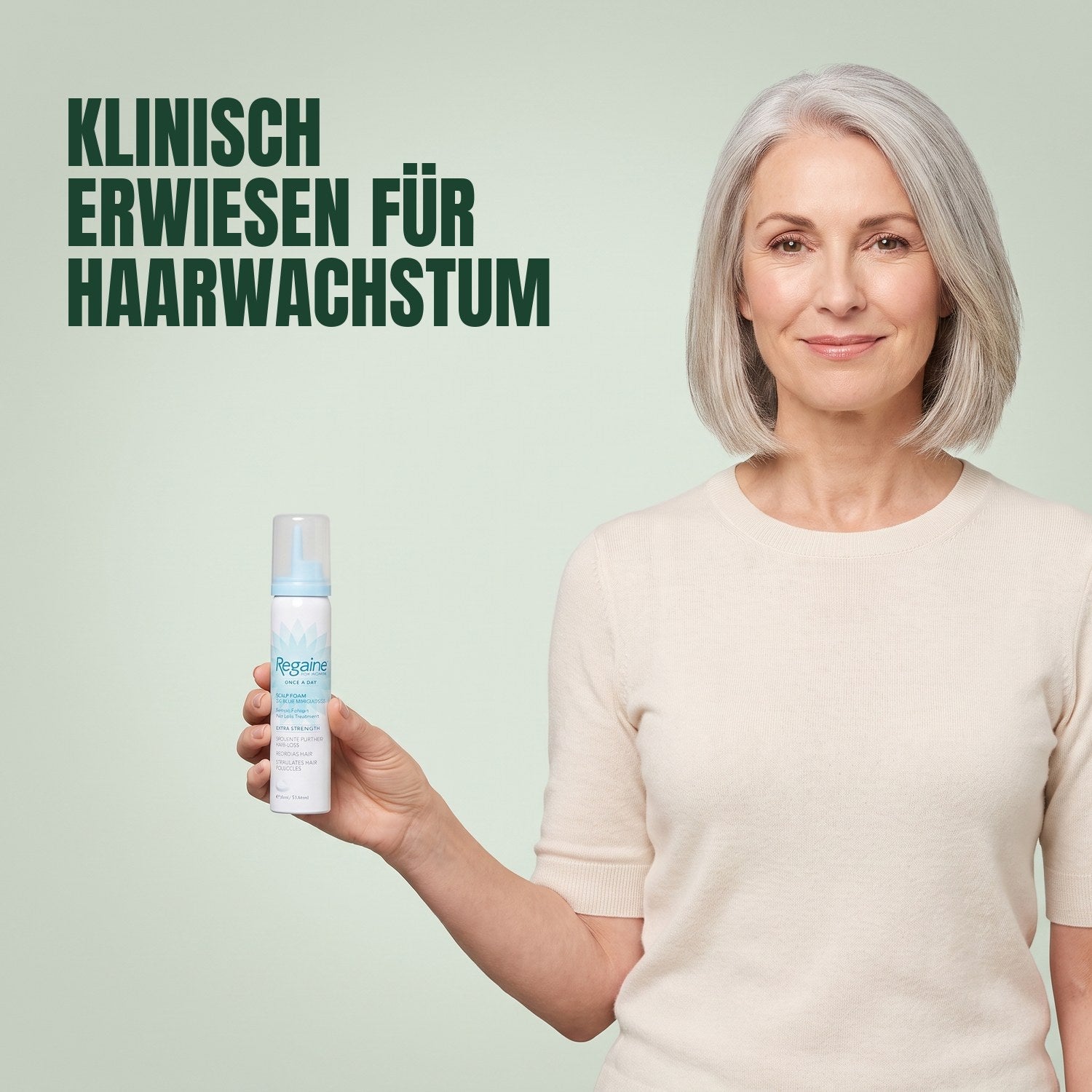 Woman holding a Regaine for Women Minoxidil 5% foam can against a green background