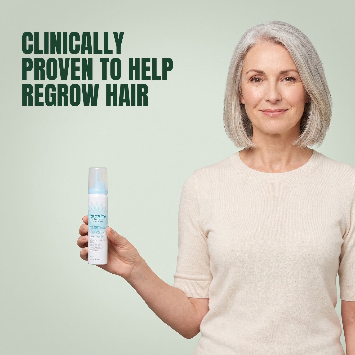 Woman holding a Regaine for Women Minoxidil 5% foam can against a green background