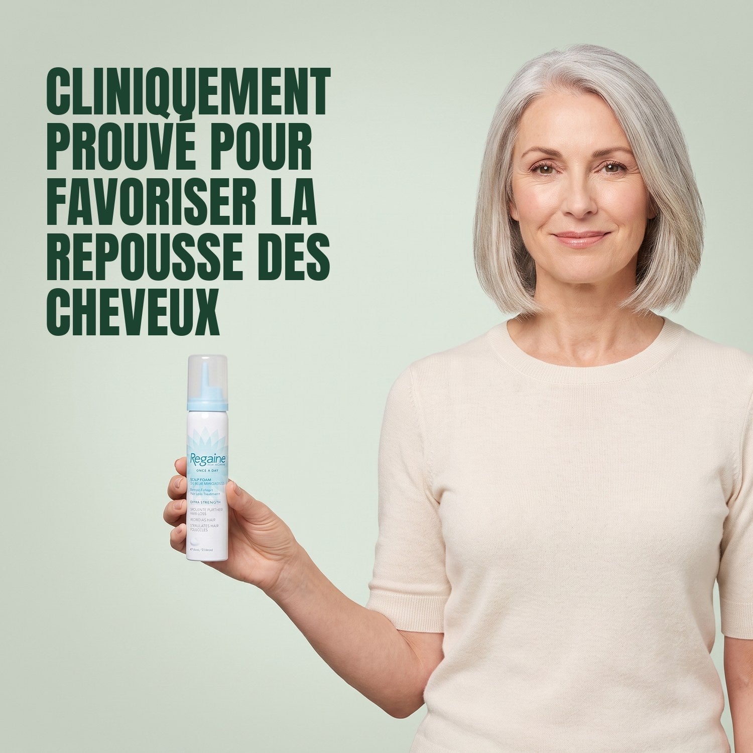 Woman holding a Regaine for Women Minoxidil 5% foam can against a green background