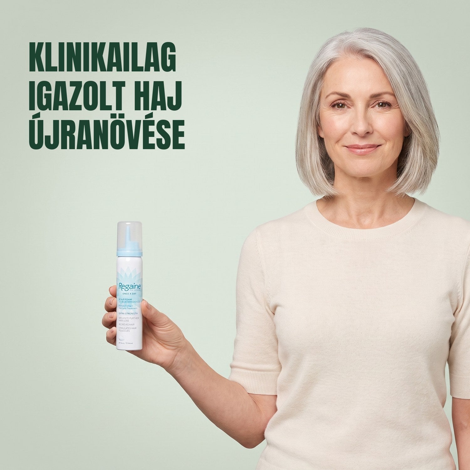 Nő a Regaine for Women Minoxidil 5% habos dobozát tartja zöld háttér előtt