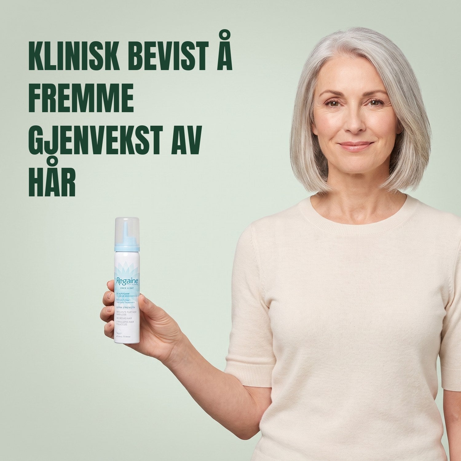 Kvinne som holder en boks Regaine for Women Minoxidil 5 % skum mot en grønn bakgrunn
