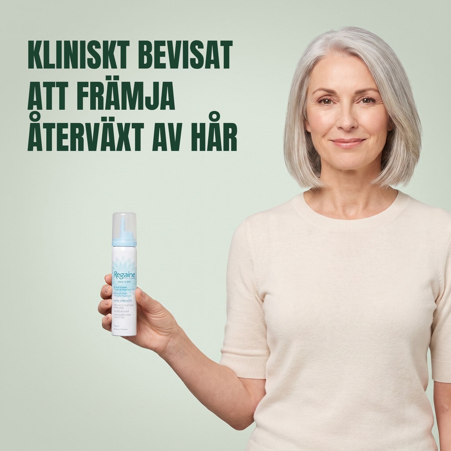 Kvinna håller en burk Regaine for Women Minoxidil 5% skum mot en grön bakgrund