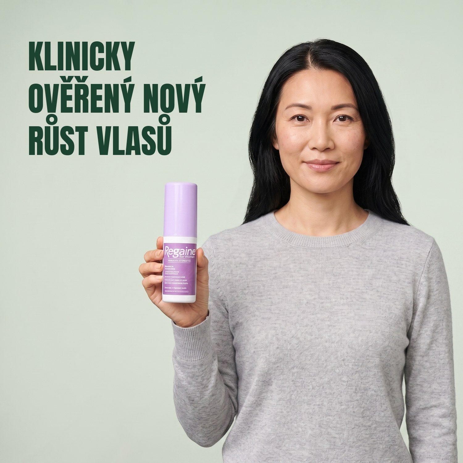 Žena drží balení roztoku Regaine for Women Minoxidil 2% na zeleném pozadí