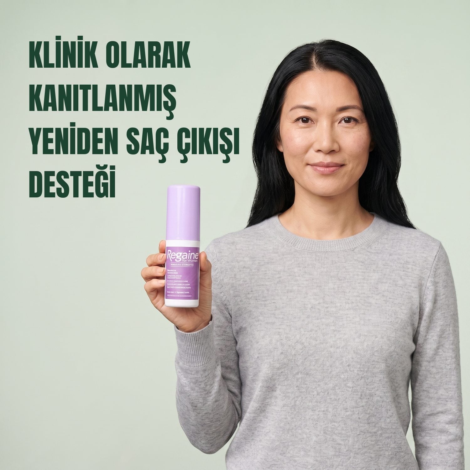 Woman holding the Regaine for Women Minoxidil 2% lotion pack against a green background