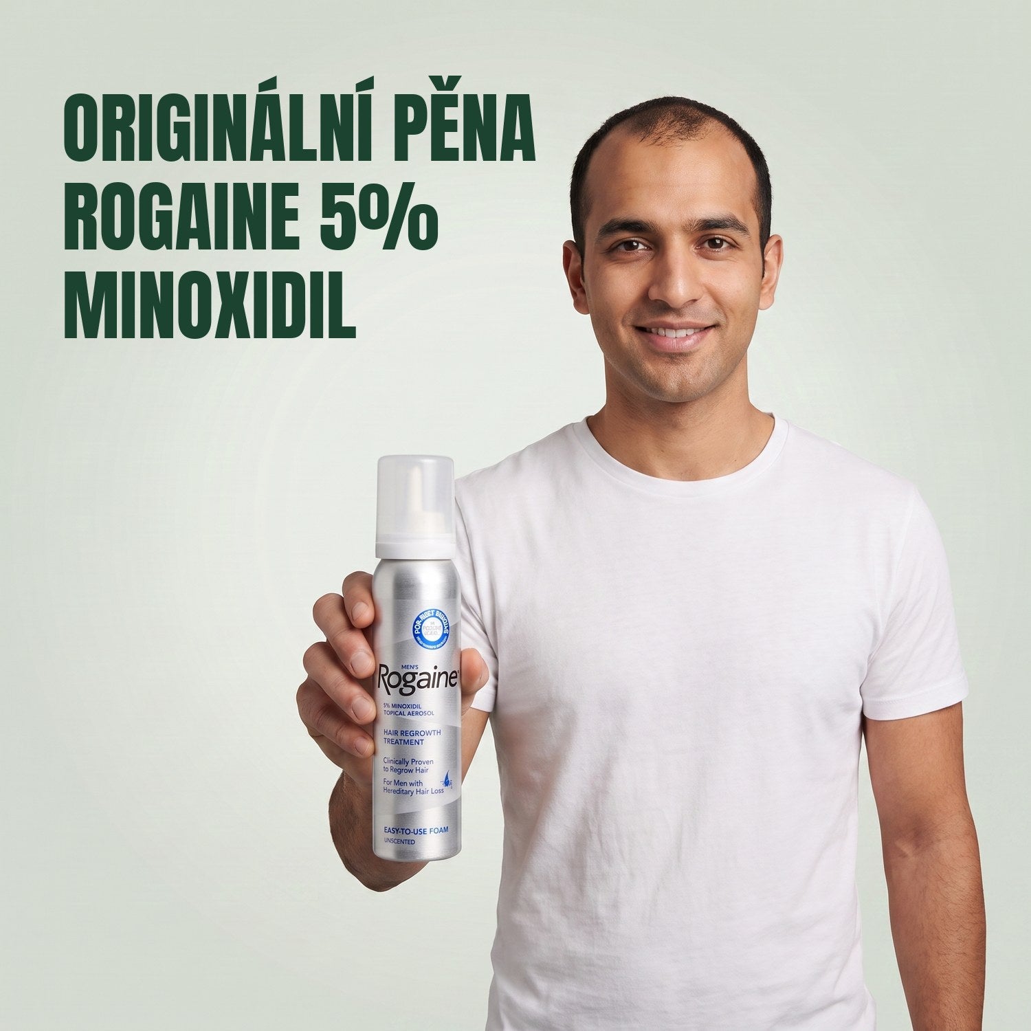 Muž drží krabičku pěny Rogaine 5% minoxidil s plechovkou pěny na zeleném pozadí