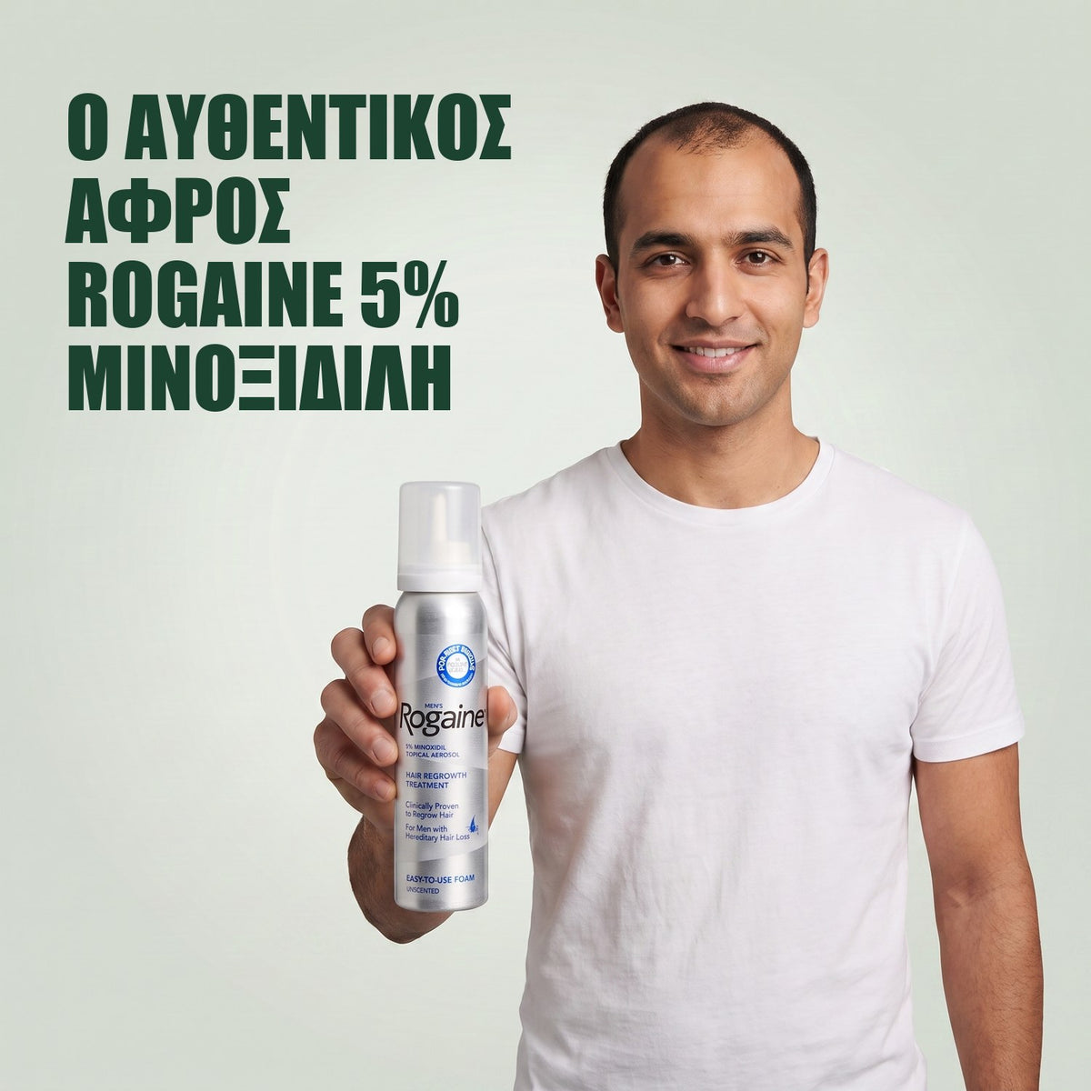 Άντρας κρατά το κουτί Rogaine 5% minoxidil αφρός με δοχείο αφρού σε πράσινο φόντο