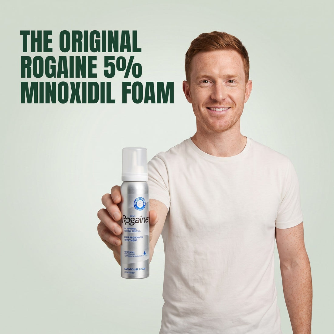 Man holding a Rogaine 5% minoxidil foam can against a green background