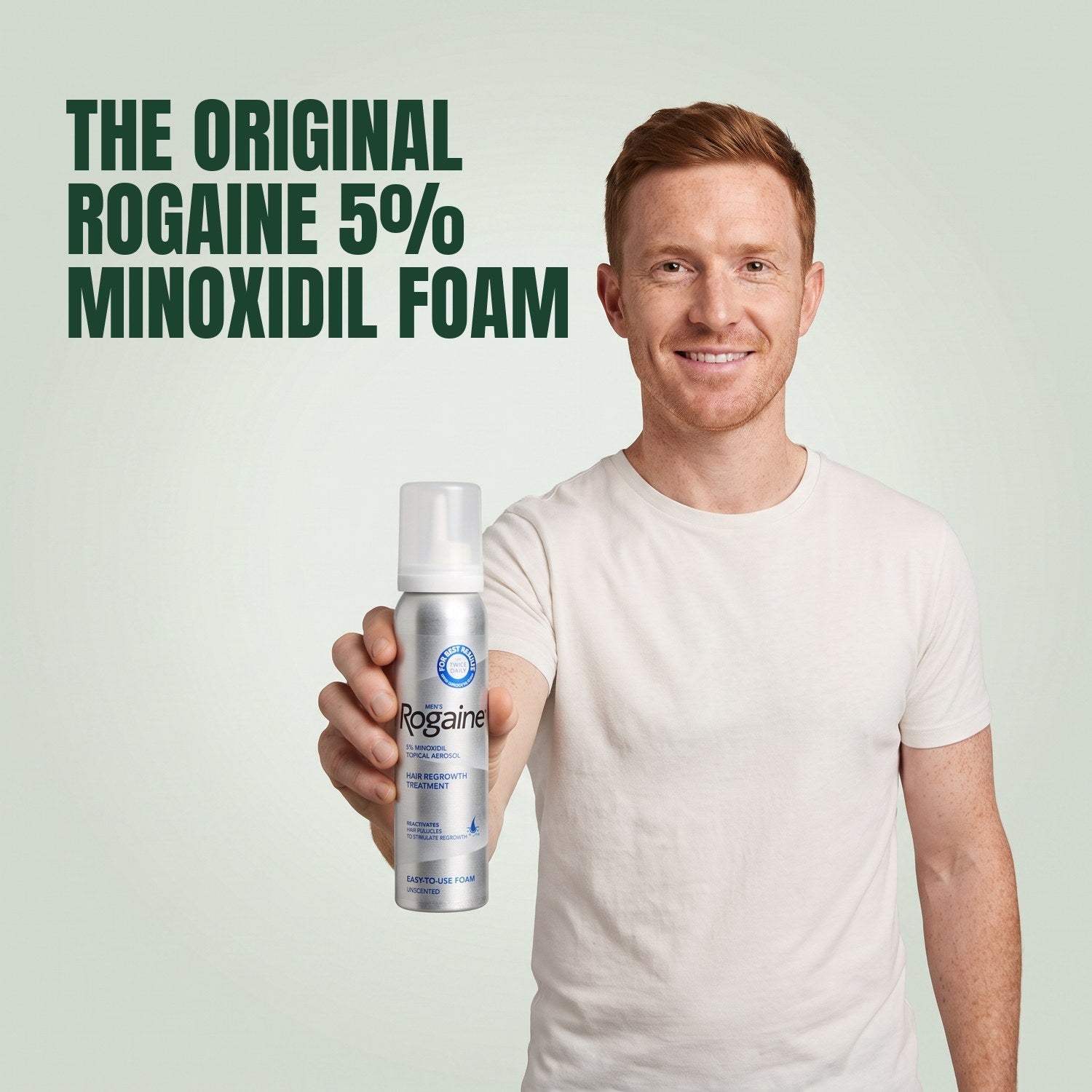 Man holding a Rogaine 5% minoxidil foam can against a green background