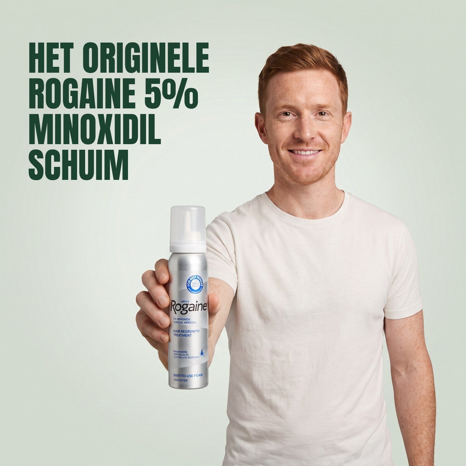 Man holding a Rogaine 5% minoxidil foam can against a green background