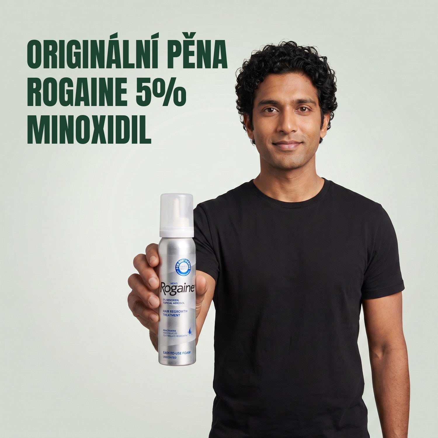 Muž drží krabičku pěny Rogaine 5% minoxidil s plechovkou pěny na zeleném pozadí