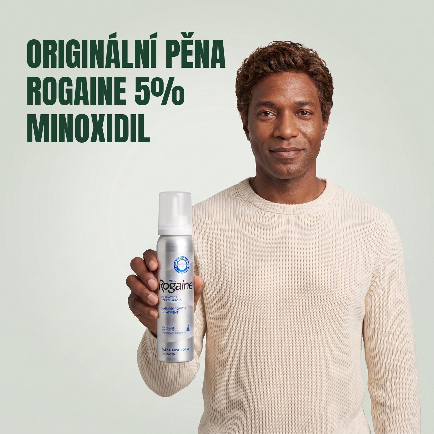 Muž drží krabičku pěny Rogaine 5% minoxidil s plechovkou pěny na zeleném pozadí