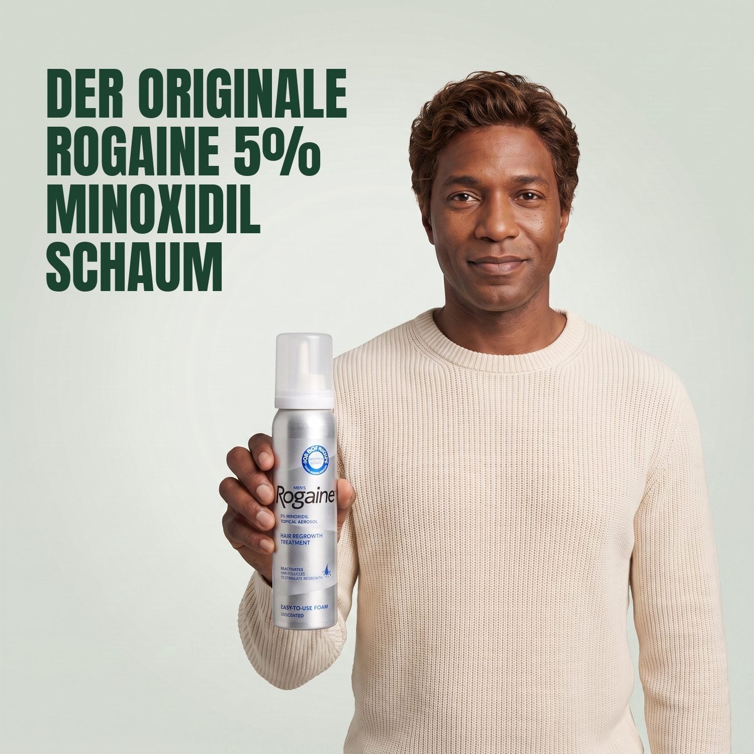 Man holding the Rogaine 5% minoxidil foam carton with a foam can against a green background