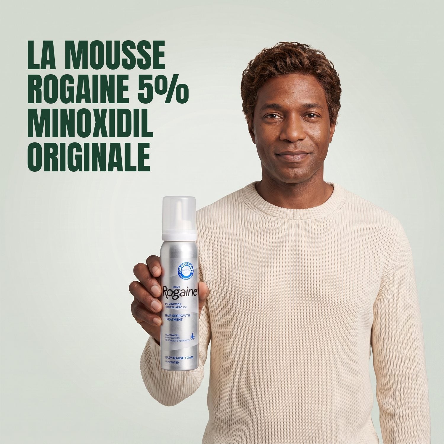 Man holding the Rogaine 5% minoxidil foam carton with a foam can against a green background