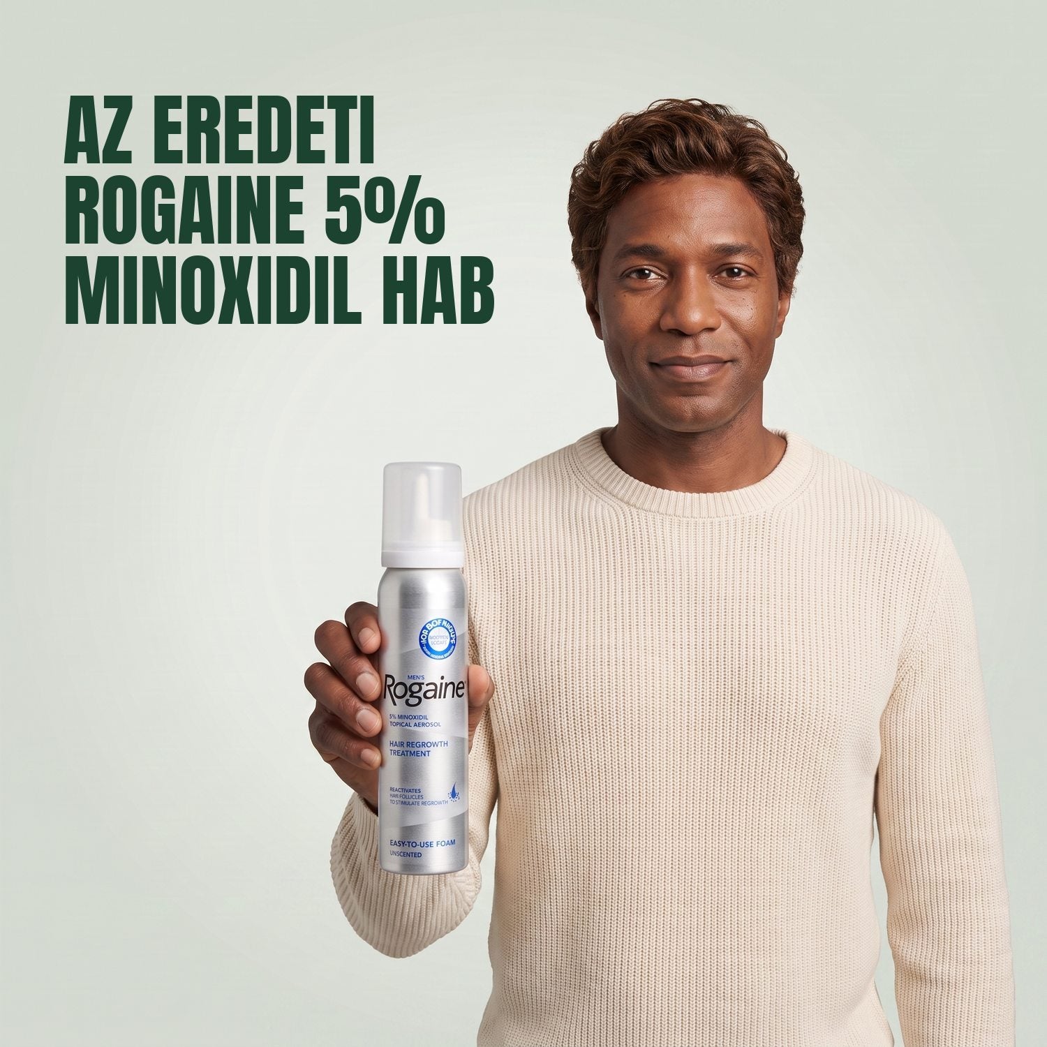 Férfi tartja a Rogaine 5% minoxidil hab csomagolását egy hab dobozzal, zöld háttér előtt