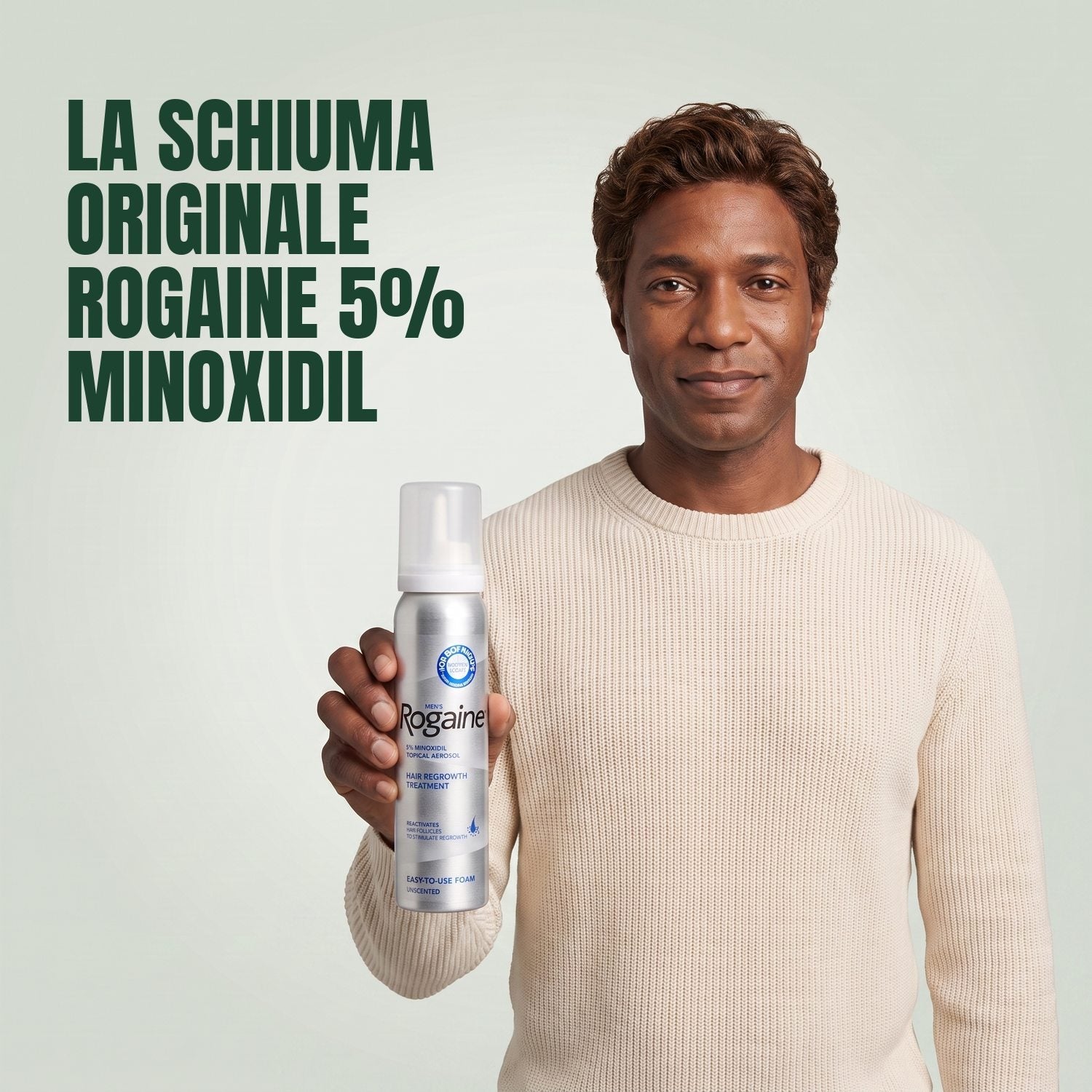 Man holding the Rogaine 5% minoxidil foam carton with a foam can against a green background