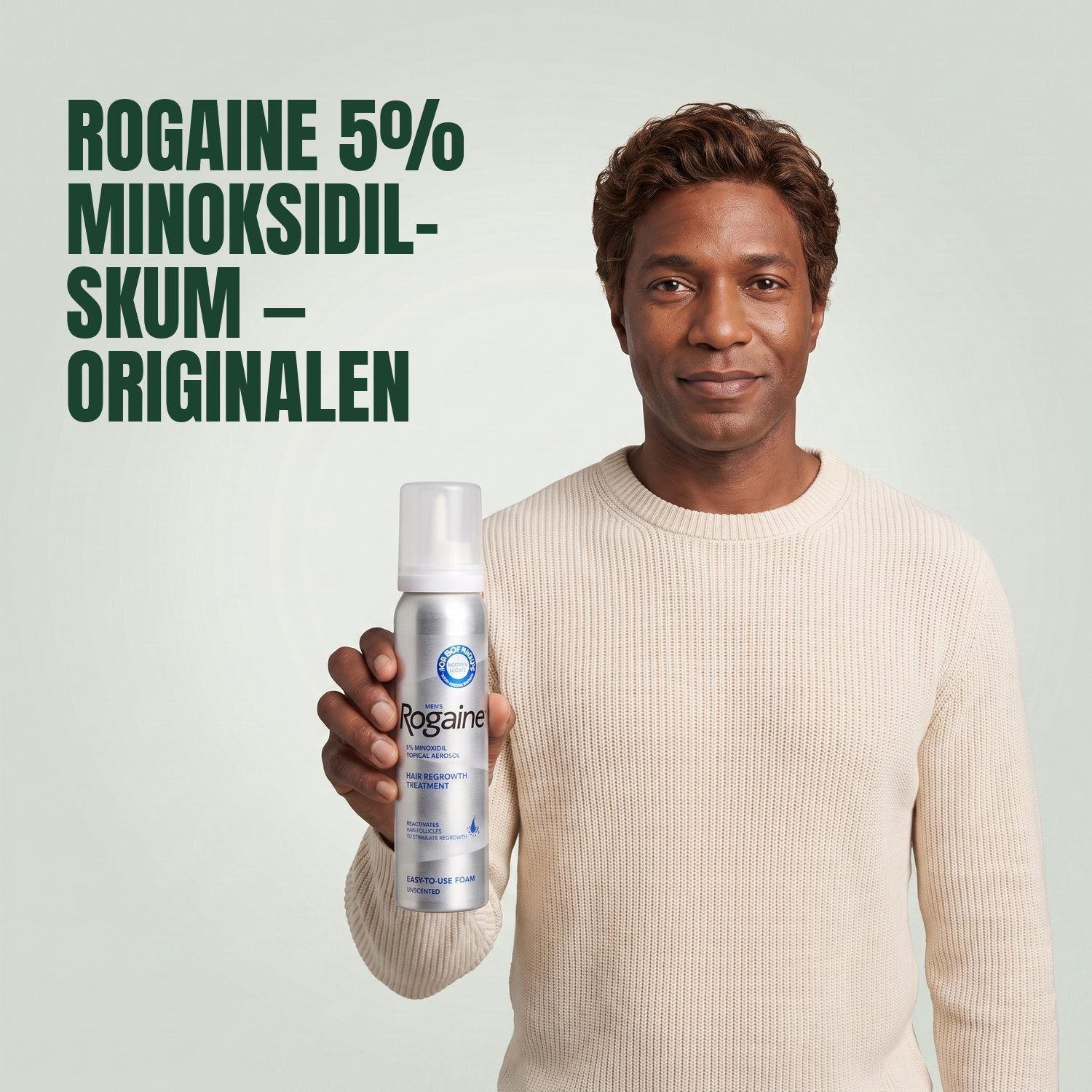 Man holding the Rogaine 5% minoxidil foam carton with a foam can against a green background