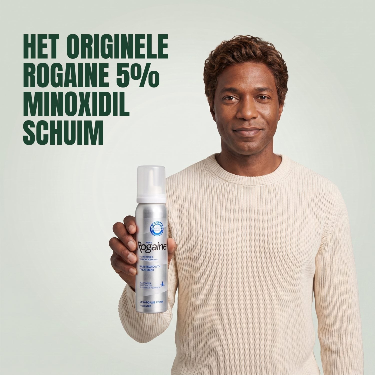 Man holding the Rogaine 5% minoxidil foam carton with a foam can against a green background