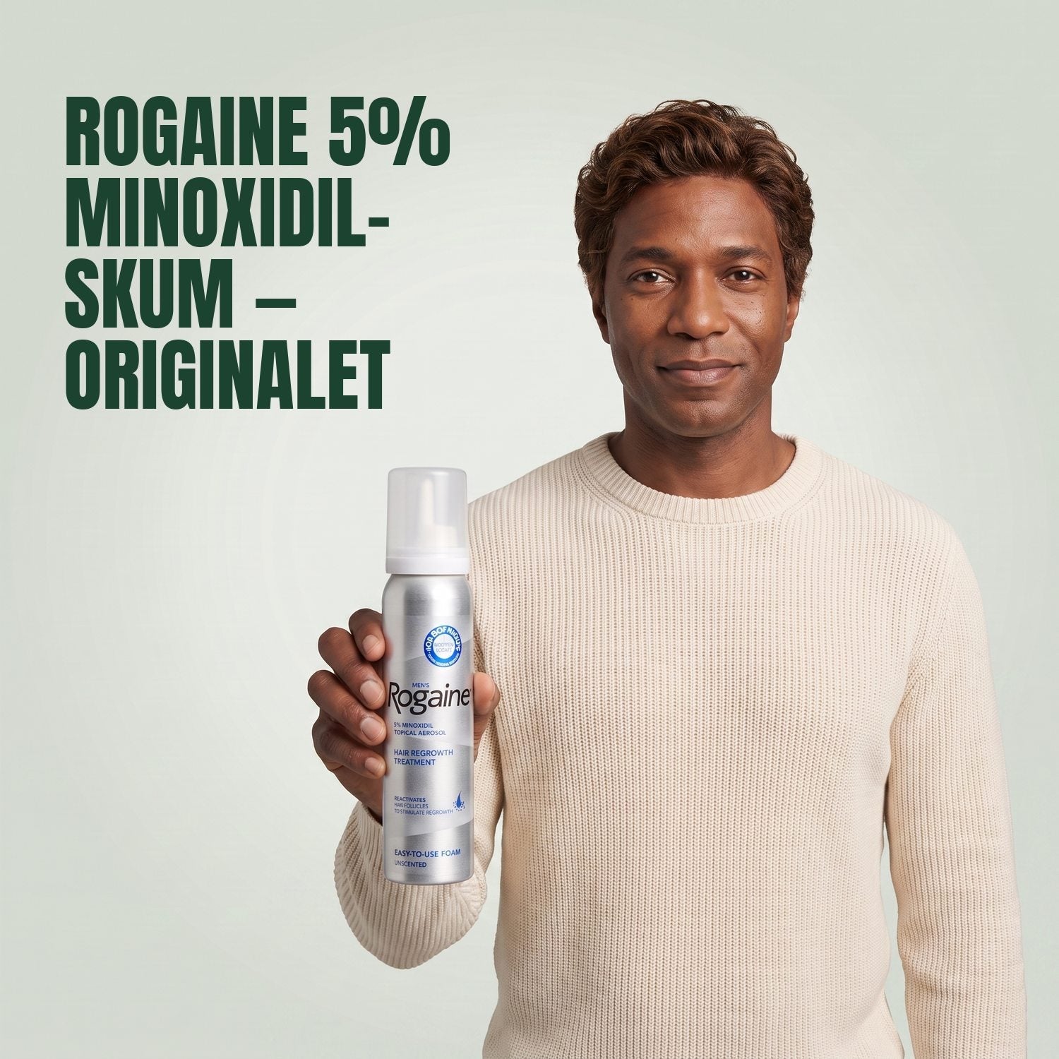 Man holding the Rogaine 5% minoxidil foam carton with a foam can against a green background